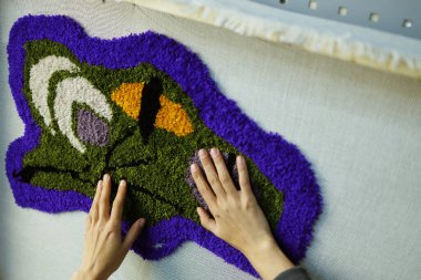 Atölyedeki tuvalde halıyı kontrol eden bir kadın. 