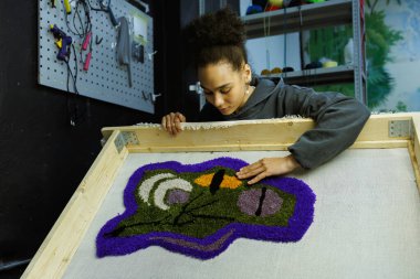 Genç Afrikalı Amerikalı zanaatkar stüdyoda el yapımı halıya bakıyor.