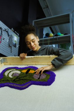 Afrikalı Amerikalı zanaatkar atölyedeki el yapımı halıya bakıyor.