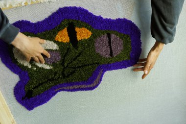 Atölyede el yapımı halıya dokunan bir kadın resmi.