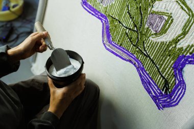 El yapımı halının yanında tutkal ve mala tutan bir kadın resmi.