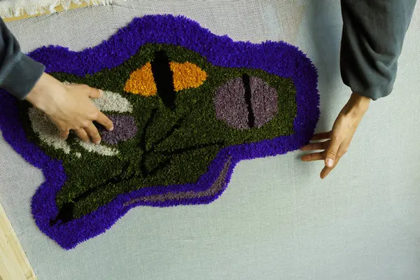 Atölyede el yapımı halıya dokunan bir kadın resmi.