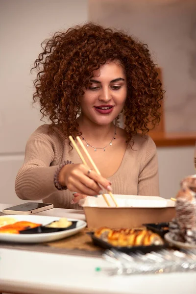 Young woman eating sushi asian food and noodles using choopsticks from take away delivery.