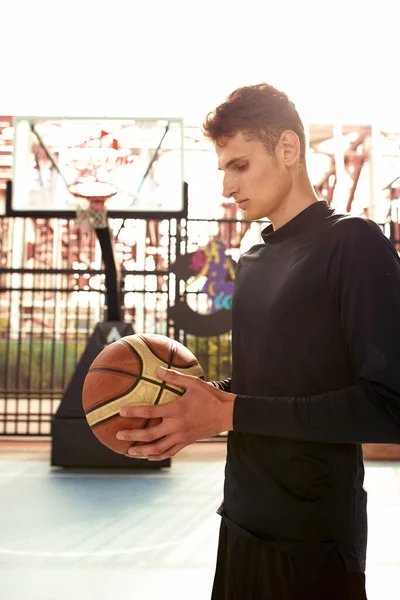 Young man with a basketball in his hands on the city basketball court.