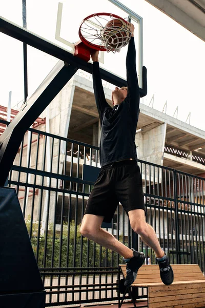 Young man with a basketball in his hands on the city basketball court.
