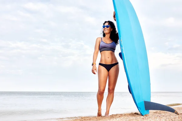 Young brunette woman with surf stands on the beach.
