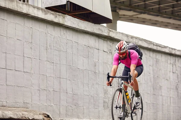 A man cyclist in glasses and a helmet rides around the city against the backdrop of a concrete wall, to work on a bike, healthy lifestyle, cycling lifestyle, cardio training in everyday life.
