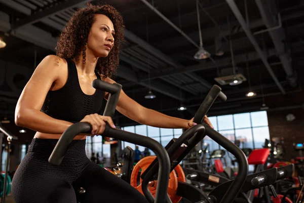 Exercise bike and black woman in the gym for training, cardio training and movement with speed, energy and motivation. Fitness girl, stationary exercise bike and air bike, wellness and action.