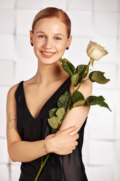 Beautiful young disabled woman with flowers in her hand, smiles cheerfully, holding a flower in her hands in a black dress. Diversity disability and flowers.