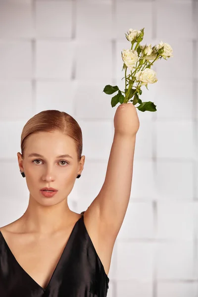 Beautiful young disabled woman with a flower instead of a hand raised up, holding a flower in her hands in a black dress. Diversity disability and flowers