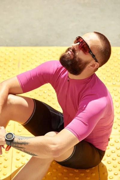 Close-up of a professional cyclist in sportswear sitting relaxing and enjoying the sun in the park, copyspace. The concept of an active and healthy lifestyle