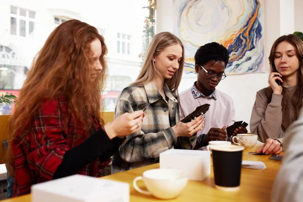 A multinational company of young people drink coffee and play games, look at smartphones, take selfies