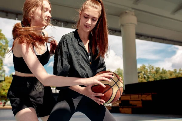 Two young women playing basketball on street court on a sunny day. Women playing a streetball game outdoors