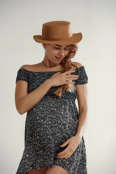 妊娠中の女性でカントリースタイル夏のドレスとわら帽子立って彼女の腹 スタジオの肖像画 — ストック写真