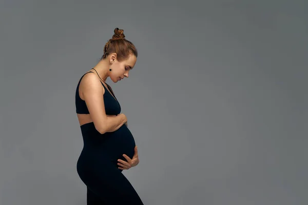 灰色で隔離された可愛い妊娠中の腹 腹部を手で抱きしめる若妻の横顔 妊娠の終わりの第三学期に大きな腹 妊娠生活の概念 — ストック写真