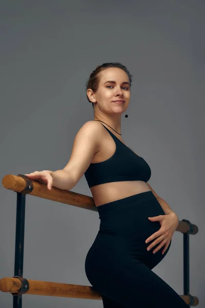 妊娠中の女性のポーズ近くのバレエスタジオで黒レギンスと上にグレーの背景 — ストック写真
