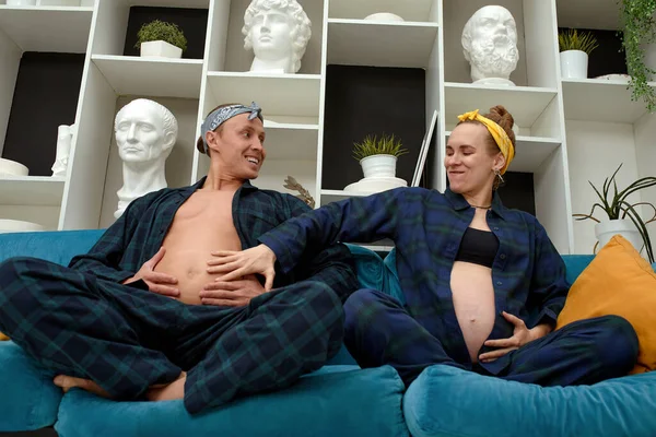 一个怀孕的女人和她的丈夫拍摄有趣的怀孕照片 那个男人坐在沙发上 露出了肚皮 — 图库照片