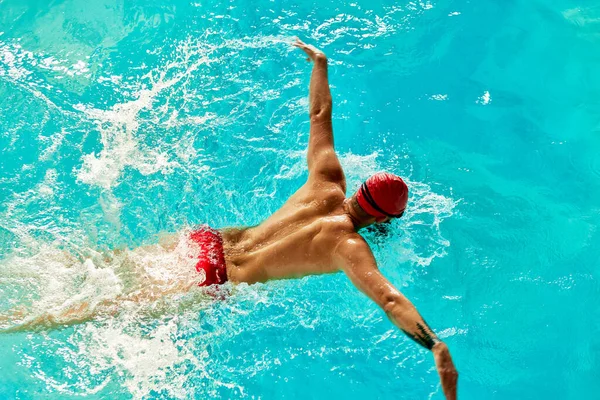 Mężczyzna Pływa Basenie Czerwonej Czapce Okularach Wśród Promieni Słońca Trenuje — Zdjęcie stockowe