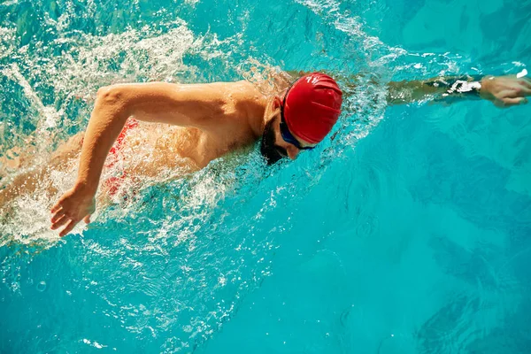 一名年轻男子戴着红帽子和泳镜在游泳池里爬泳 在游泳池里训练 准备比赛 前爬泳 — 图库照片
