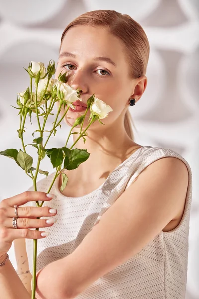 A young woman with special needs with flowers in her hand, a girl born without a hand, in white dress on a white background in the rays of the sun beauty fashion concept.