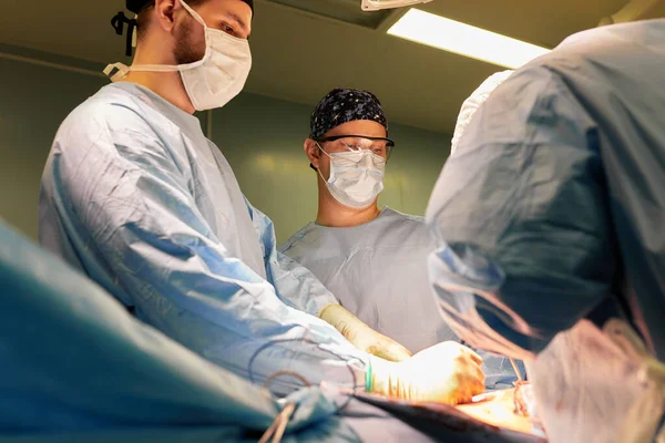 两名经验丰富的外科医生和一名警觉的护士在现代手术室明亮的电灯下做手术 一名专业外科医生在与癌症作斗争时被枪击身亡 — 图库照片