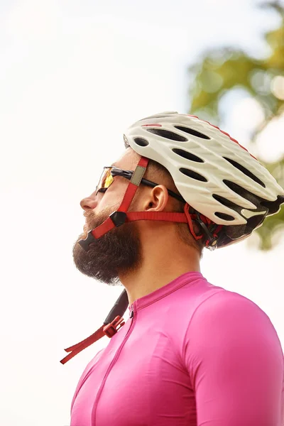 强壮的男性骑自行车者穿着运动服 戴着眼镜 戴着防护头盔 骑着自行车在森林里散步 骑马后休息一下 背景是蓝天 — 图库照片