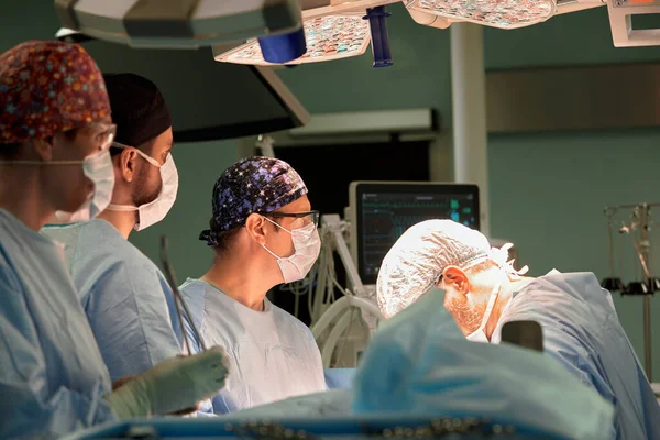 Shot of two experienced surgeons and an alert nurse performing an operation under a bright electric lamp in a modern operating room, professional surgeons, fighting cancer.