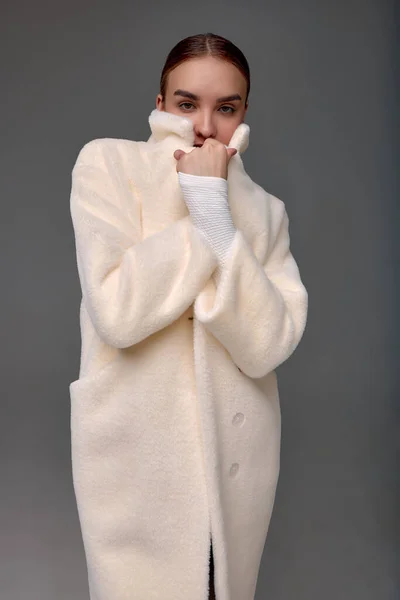 灰色の背景に薄手の人工毛皮のコートを着た女の子 フェイクファーで作られた毛皮のコートのための現代的なファッショントレンド グレーの背景に薄毛のコートに身を包んだモデル — ストック写真