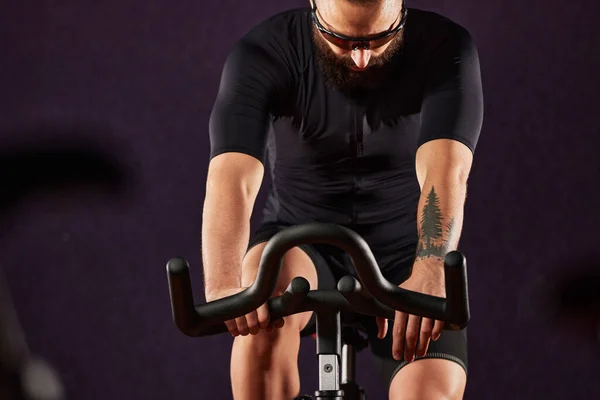Portrait of a man on an exercise bike in the gym, a man with a beard and glasses on an exercise bike. Fitness man using exercise bike during cardio workout in crossfit gym