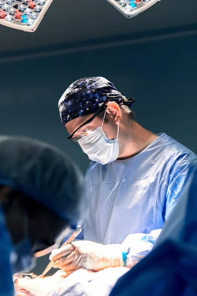 男外科医生在暗色手术室进行手术 手术背景为一盏灯 现代手术室的专业外科医生进行手术切除肉瘤 — 图库照片