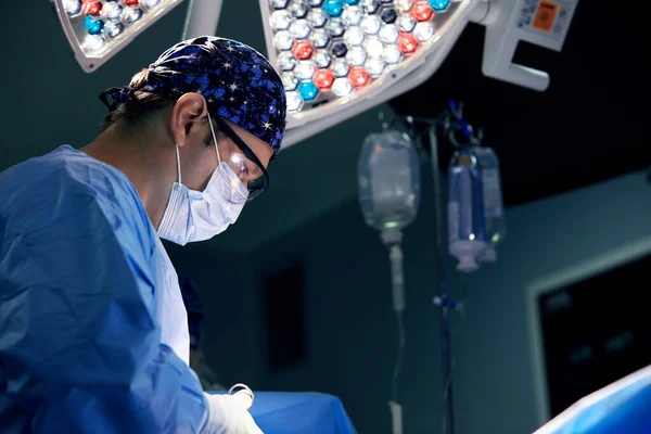 男外科医生在暗色手术室进行手术 手术背景为一盏灯 现代手术室的专业外科医生进行手术切除肉瘤 — 图库照片
