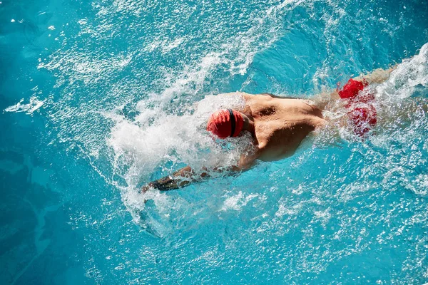 男子游泳者游泳蛙泳 男子戴着红色泳帽和游泳护目镜在游泳池游泳时的近照 — 图库照片
