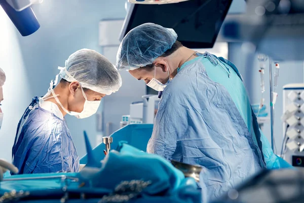 stock image The team of surgeons in the operating room bent over the patient, complex surgical operation, high-tech medicine, life saving.