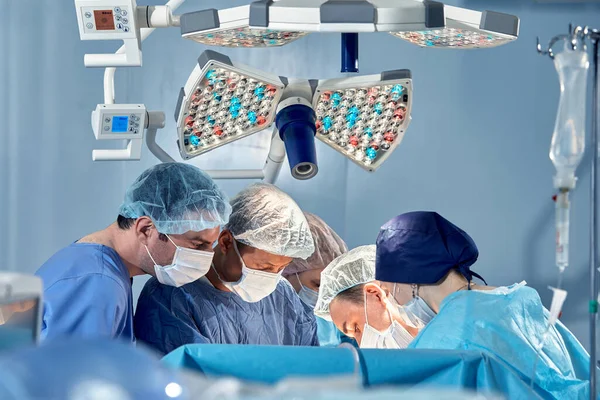 stock image The team of surgeons in the operating room bent over the patient, complex surgical operation, high-tech medicine, life saving.
