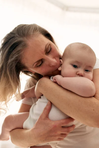 妈妈在明亮的孩子房间里拥抱和亲吻她的孩子 妈妈小心地把婴儿抱在怀里 快乐的童年 — 图库照片