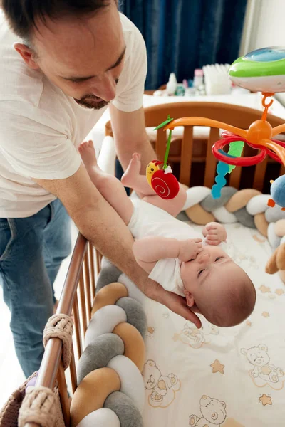 一个快乐的父亲把他的孩子放在婴儿床里 慈爱的父亲温柔而小心地把孩子抱在怀里 — 图库照片