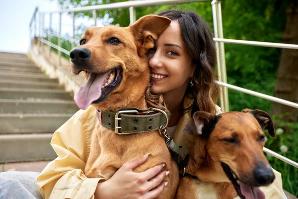 Young charming smiling girl is resting while walking in the park with two golden dogs. The girl hugs her pets. Love and affection between owner and pet. Adopting a pet from a shelter