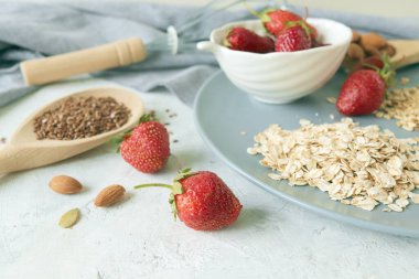 Yulaf ezmesi, tabakta taze çilek, kuru üzüm, fındık ve tohum, masada sağlıklı kahvaltı malzemeleri.