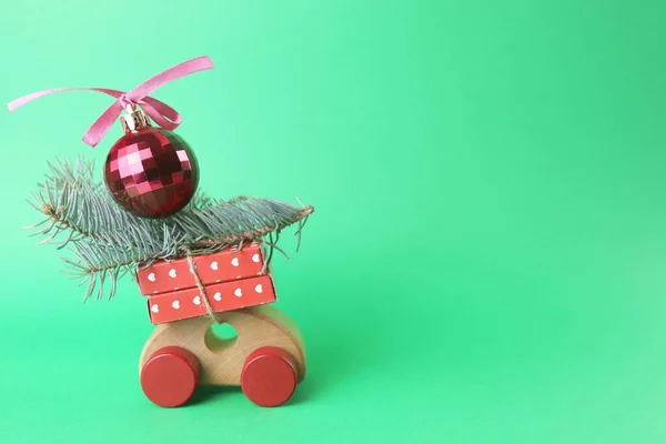 圣诞节 一辆包装着礼物和云杉树枝的玩具车 一个有蝴蝶结的红球 一个绿色背景的玩具房子 祝贺的概念 一张明信片 — 图库照片