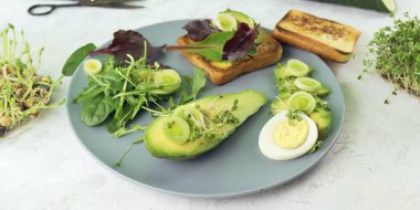 Sandwiches with avocado, boiled eggs, leek and arugula, sprinkled with fresh micro green sprouts, on a wooden board, natural ingredients, healthy food