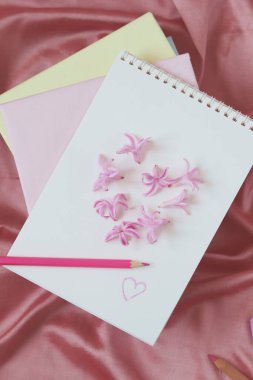 A blank page of a notebook is decorated with fresh hyacinth flowers, in the shape of a heart, on the background of natural silk fabric, stacks of books, the concept of love emotion, Valentine's Day, congratulation, gift 