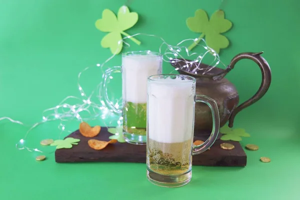 Patrick\'s Day, foamy beer in glass mugs, chips and cookies, green shamrocks and gold coins, on a wooden background, party, St. Patrick\'s Day celebration
