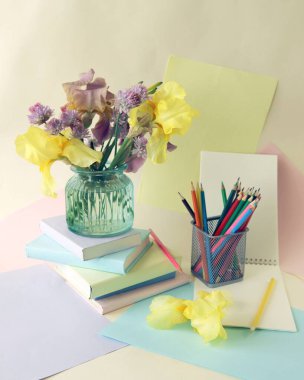 Okula, sanat malzemelerinin durgun hayatına, kitap yığınına, ders kitaplarına, pastel renkli kağıdın üzerinde bir buket taze irise.
