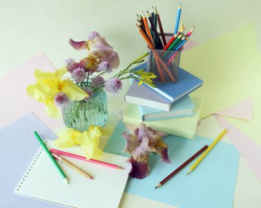 Okula, sanat malzemelerinin durgun hayatına, kitap yığınına, ders kitaplarına, pastel renkli kağıdın üzerinde bir buket taze irise.
