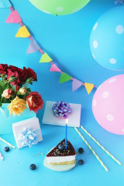 Mumlar, çiçekler, balonlar ve mavi arka planda hediye kutusu olan doğum günü pastası.