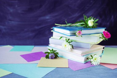 Tahta bir masanın üzerinde çiçek ayracı olan bir yığın kitap, bir karatahtanın arka planına karşı, kağıt. Okul konseptine dönelim..