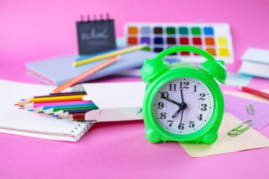 Renkli kalemler, çıkartmalar, çalar saat ve pembe arka plandaki not defteri ile okul konseptine geri dönelim.