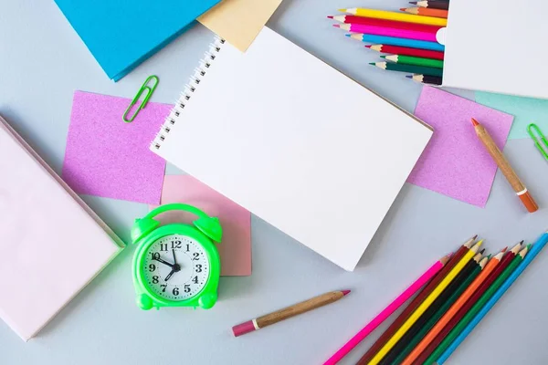 Back to school, alarm clock, colorful sticky notes and colorful pencils, drawing supplies on gray background with copy space, top view, flatly