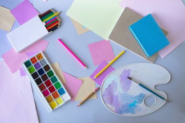 Okula, suluboya resimlere, fırçalara, renkli kalemlere, palete, gri arka planda okul gereçlerine, üst manzaraya. 