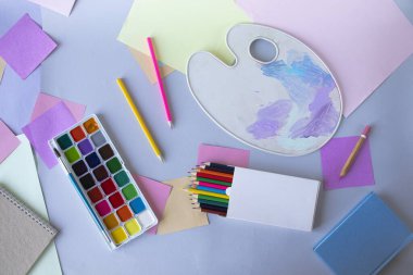 Okula, suluboya resimlere, fırçalara, renkli kalemlere, palete, gri arka planda okul gereçlerine, üst manzaraya. 